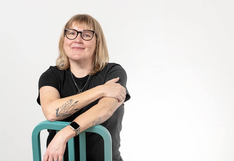 Person with tattoos and glasses leaning on a chair